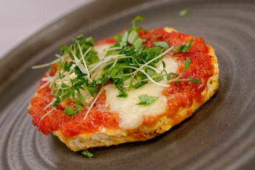 Mini-Margerita-Pizza mit Tomatensauce, geschmolzenem Käse und frischen Microgreens auf dunklem Teller